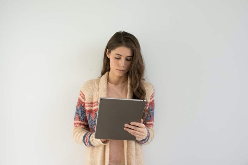 Mulher de suéter bege, cinza e vermelho segurando um tablet prateado