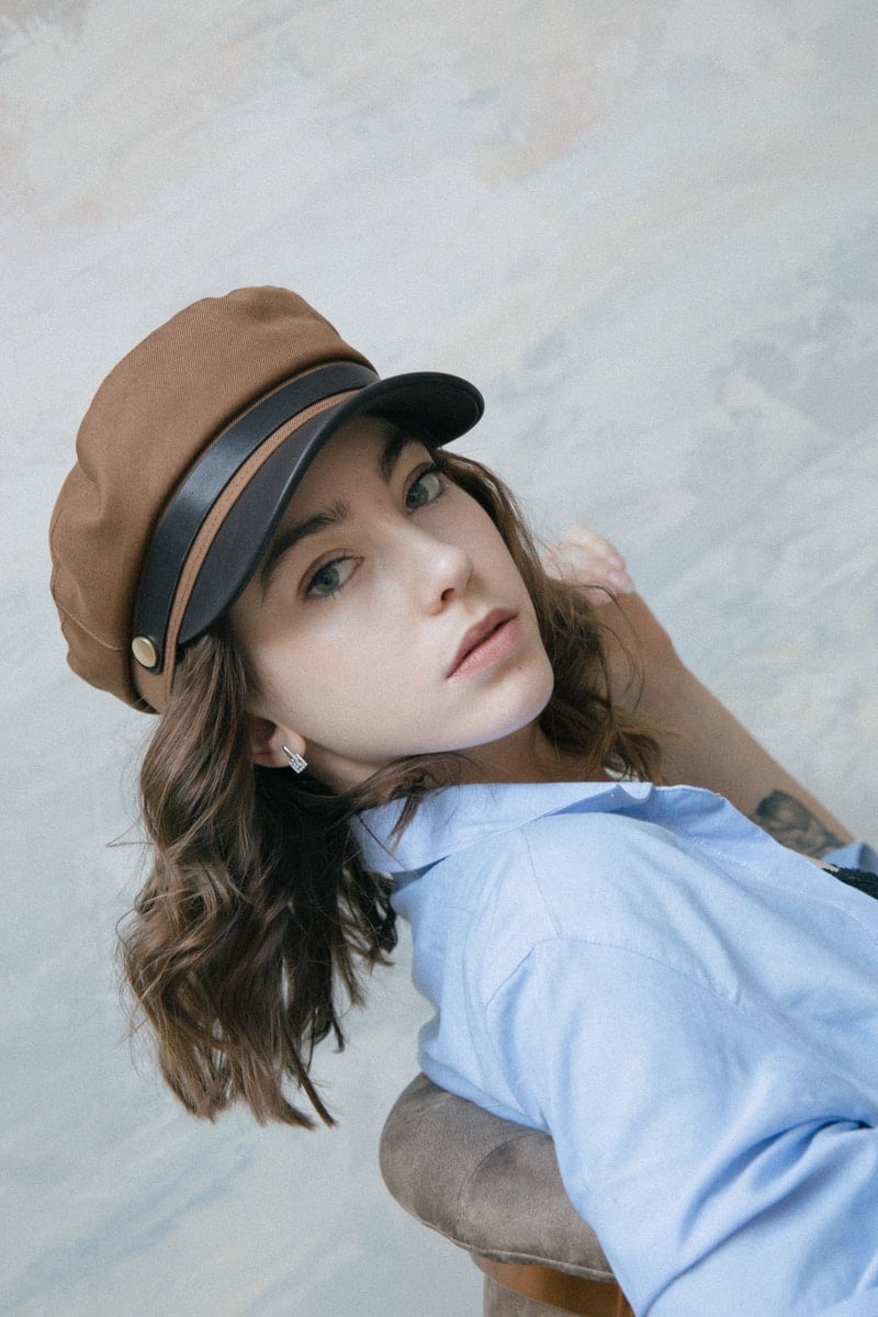 Mulher de camisa branca usando chapéu fedora preto e marrom