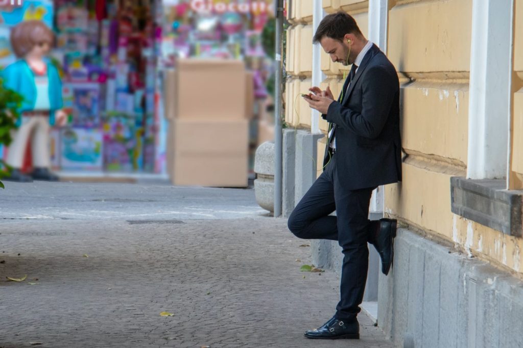 Mann hält sein Telefon und lehnt sich an ein Gebäude