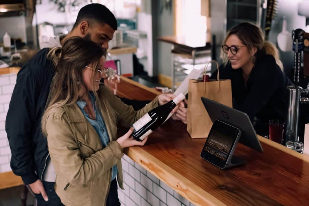 mulher segurando garrafa de vinho ao lado de homem sorrindo na frente da mulher