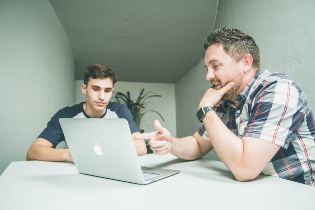 رجل يرتدي قميصا رياضيا أبيض وأسود منقوشا بأزرار يشير إلى جهاز MacBook الفضي