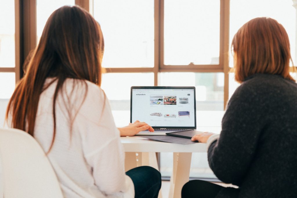 duas mulheres a falar enquanto olham para um computador portátil