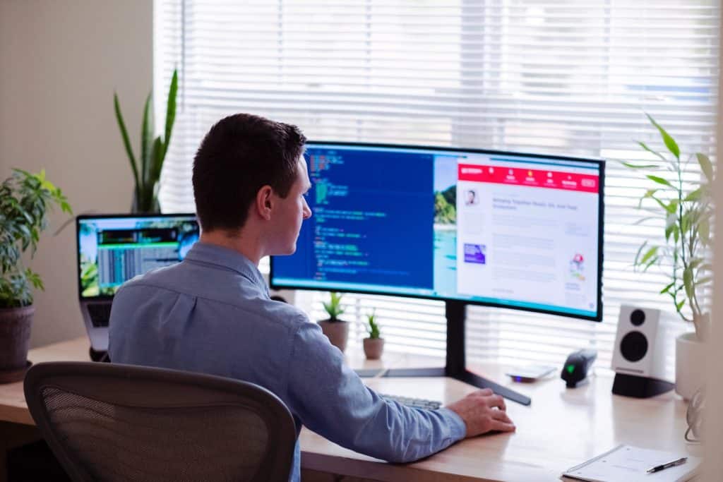 hombre con camisa de vestir gris sentado en una silla delante de un monitor de ordenador